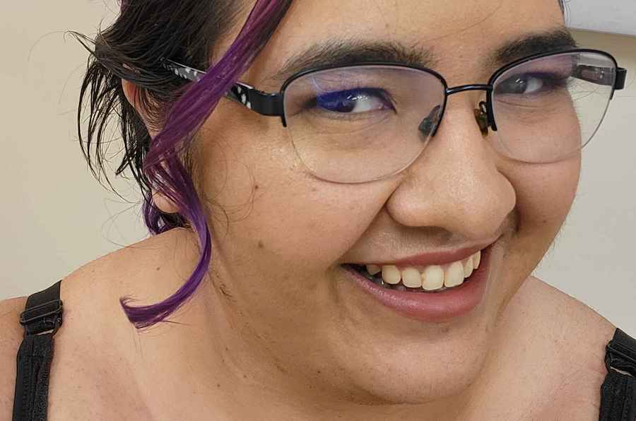 A young woman wearing glasses, with purple hair tied up in a bun. She is smiling and her head is at a 3/4 angle.