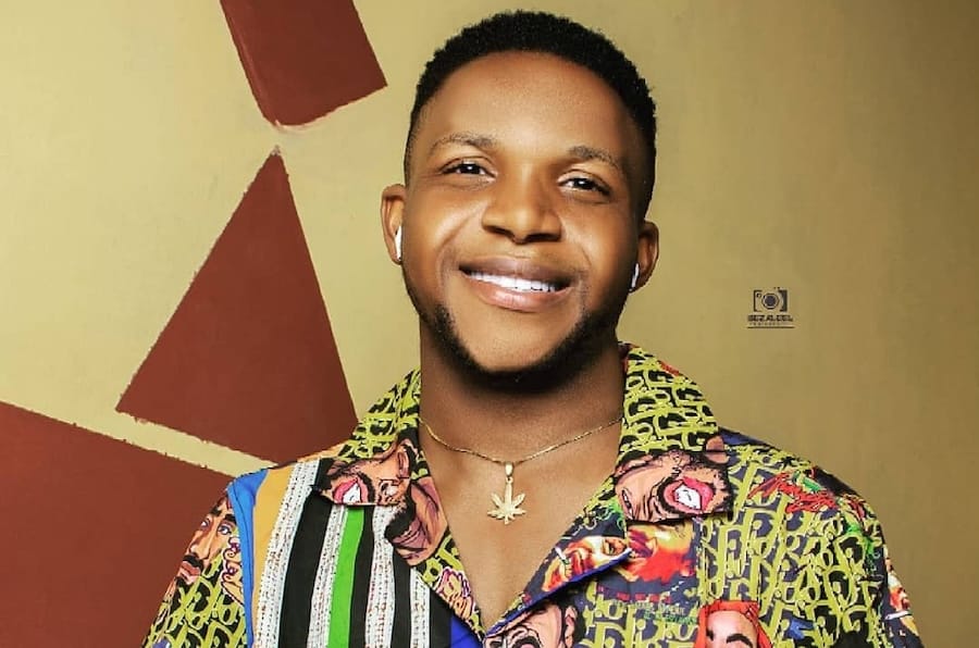 Samuel, a blxck boy by heritage and not complexion, sits on the only chair in his study room, wearing a smirk, multi-colered T-shirt, a wrist watch & a neck chain.
